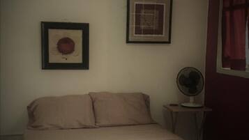 A bedroom with a bed, a wall-mounted fan, and two framed pictures.