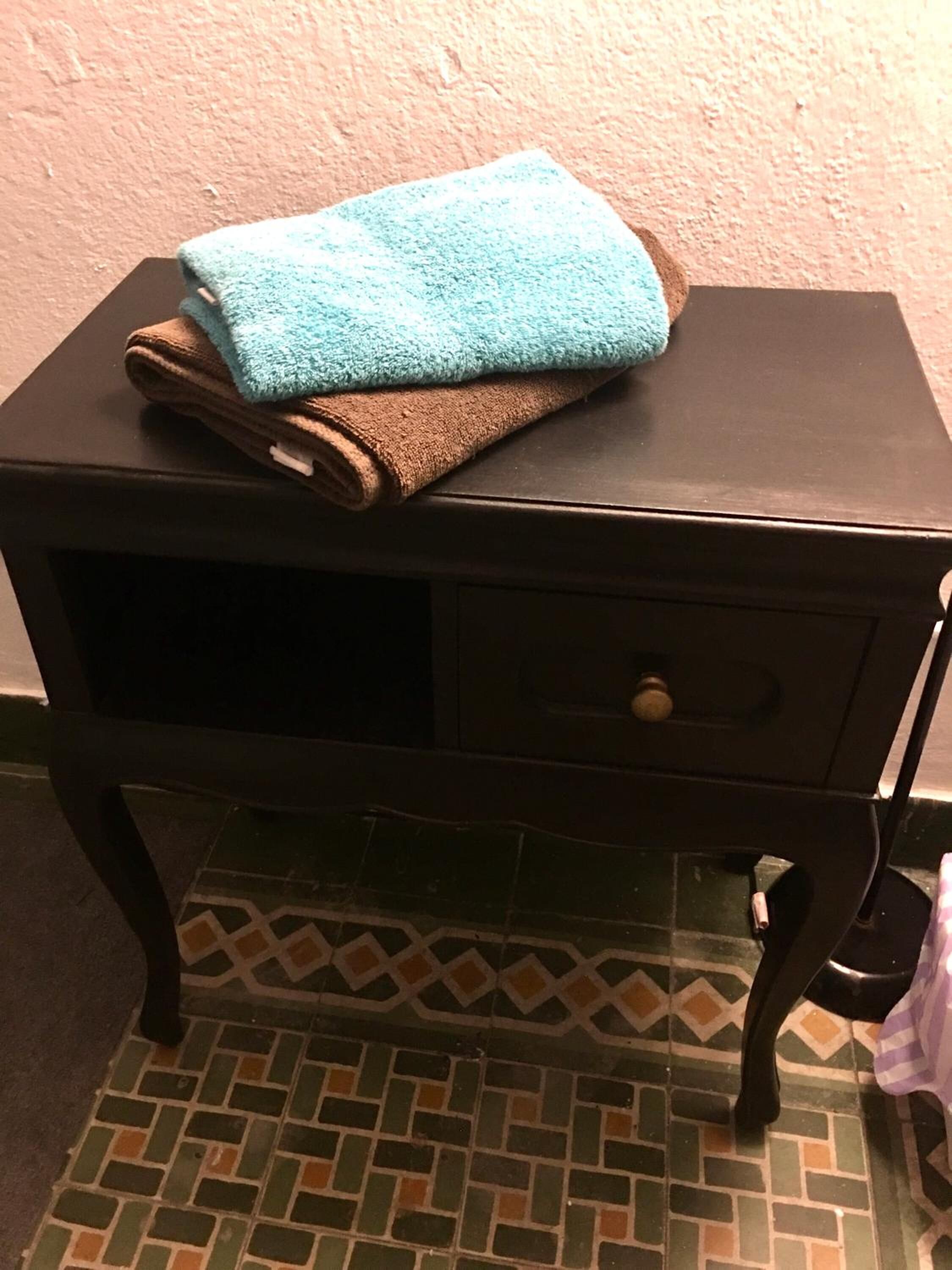 Una mesita de noche de madera pequeña con un cajón y una toalla encima.