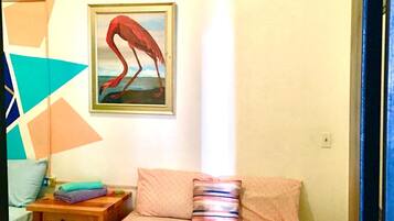 A bedroom with a bed, pillows, a nightstand, a painting of a flamingo, and a geometric wall decoration.