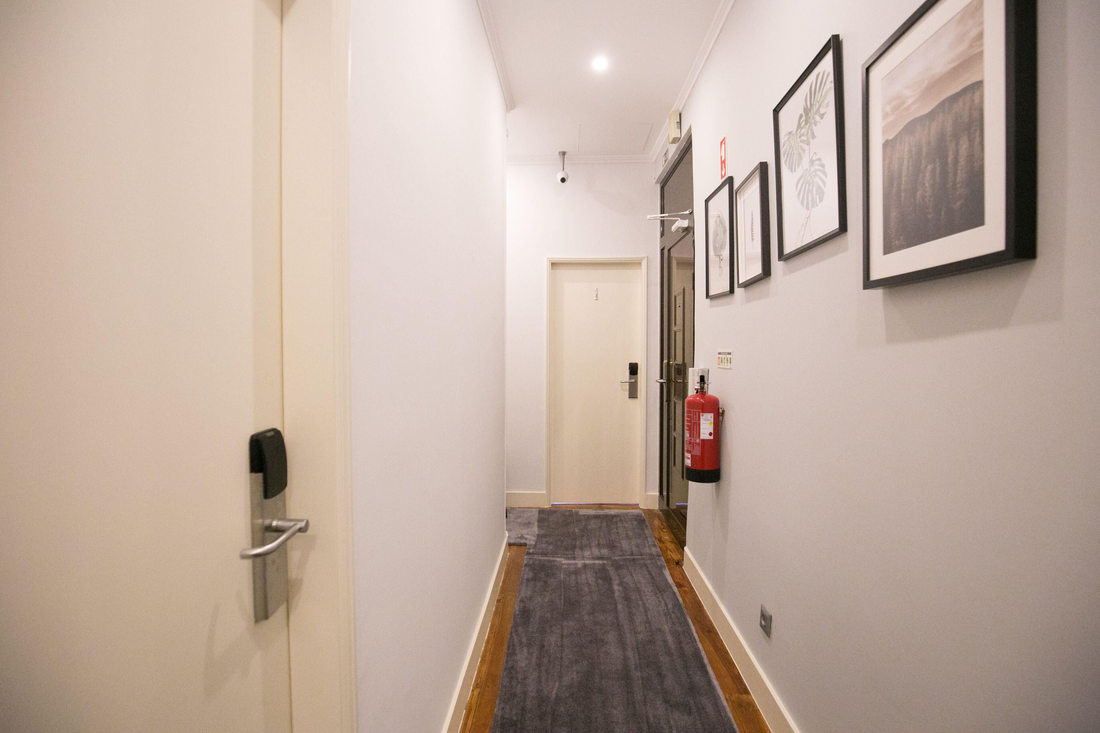 A hallway with a fire extinguisher, a door, and framed pictures on the wall.
