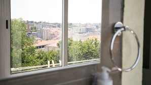 A bathroom with a window view of a cityscape, a towel ring, and a soap dispenser. - Bhuiyan Family Host (Lisbon)