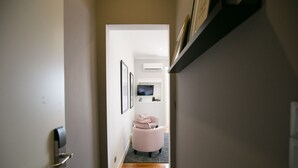 A narrow hallway with a wooden floor, a door with a modern lock, and a pink chair with a cushion. - Bhuiyan Family Host (Lisbon)
