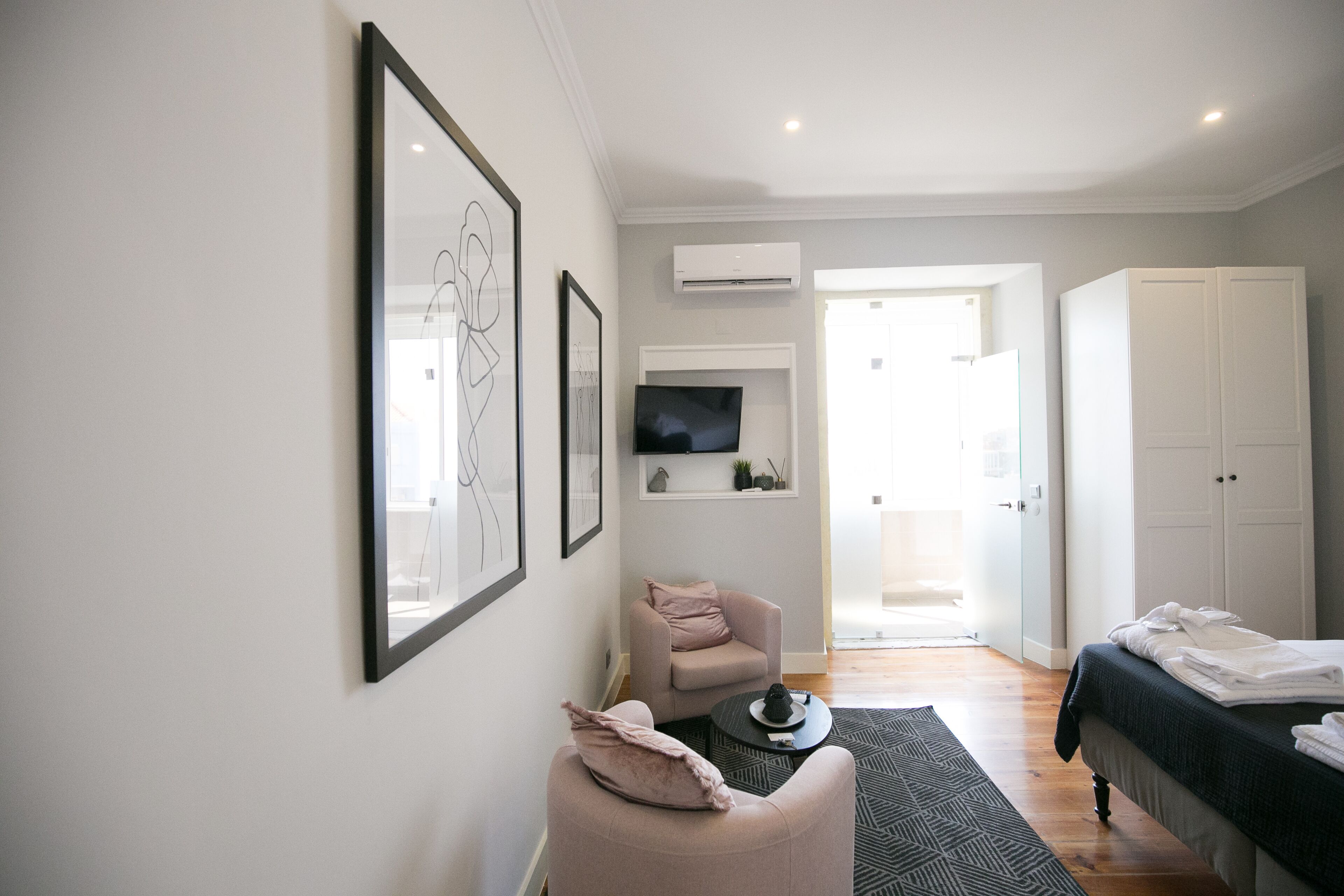 Un dormitorio moderno con una cama, una zona de estar con una silla, un televisor de pantalla plana montado en la pared y un equipo de aire acondicionado.