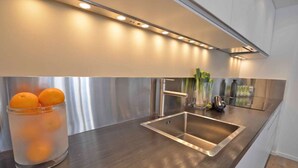 A modern kitchen with a stainless steel sink, a glass container with oranges, and a vase with green plants.