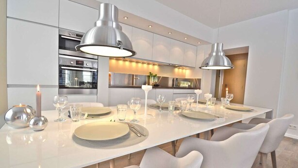A modern kitchen with stainless steel appliances, a long dining table set with white plates, and pendant lighting.