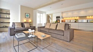 A modern living room with two sofas, a coffee table, and a kitchen in the background.