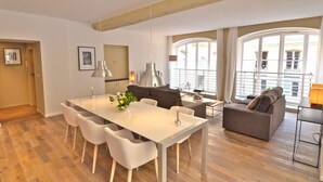 A spacious living area with a dining table, chairs, a sofa, and a balcony with large windows.