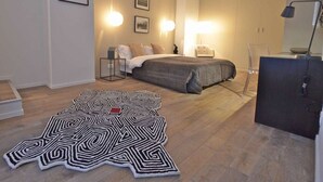 A modern bedroom with a bed, bedside lamps, a desk, and a patterned rug.