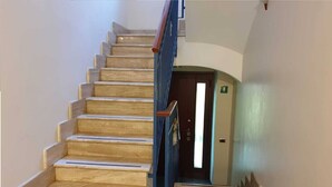 A wooden staircase with blue handrails leading to a door with an emergency exit sign. - Villa Luzzatti Hostel (Rome)