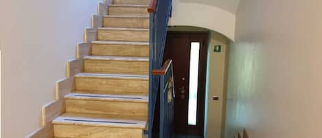 A wooden staircase with blue handrails leading to a door with an emergency exit sign.