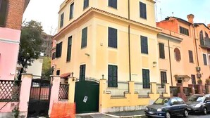 A multi-story building with a yellow facade, a gated entrance, and parked cars in front. - Villa Luzzatti Hostel (Rome)