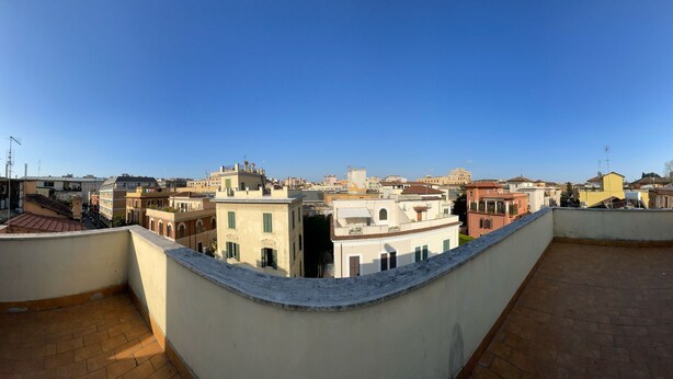 A rooftop terrace with a view of a cityscape, featuring buildings with varied architectural styles and a clear blue sky. - Villa Luzzatti Hostel (Rome)