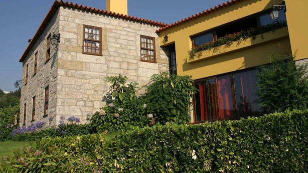 A stone building with a red-tiled roof, a yellow facade, and a balcony with potted plants. - Quinta Do Pomarinho (Arouca)