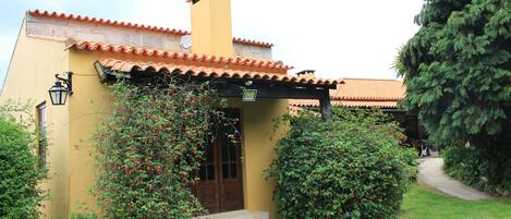 A yellow building with a tiled roof, a chimney, and a door with steps leading up to it.