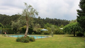 A swimming pool surrounded by a grassy lawn, trees, and a swing set. - Quinta Do Pomarinho (Arouca)