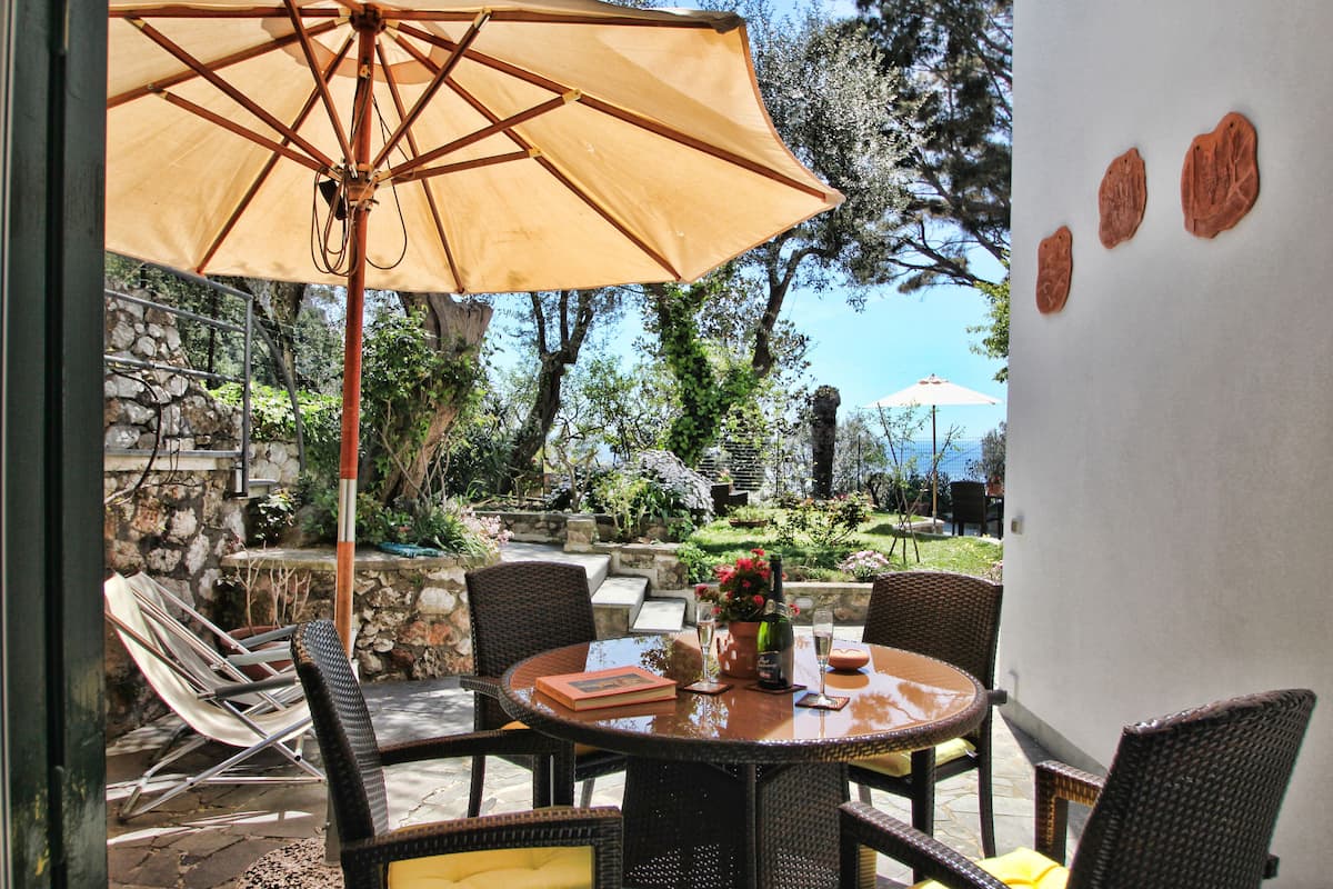 Eine Terrasse im Freien mit Korbstühlen, einem runden Tisch und einem großen Sonnenschirm.