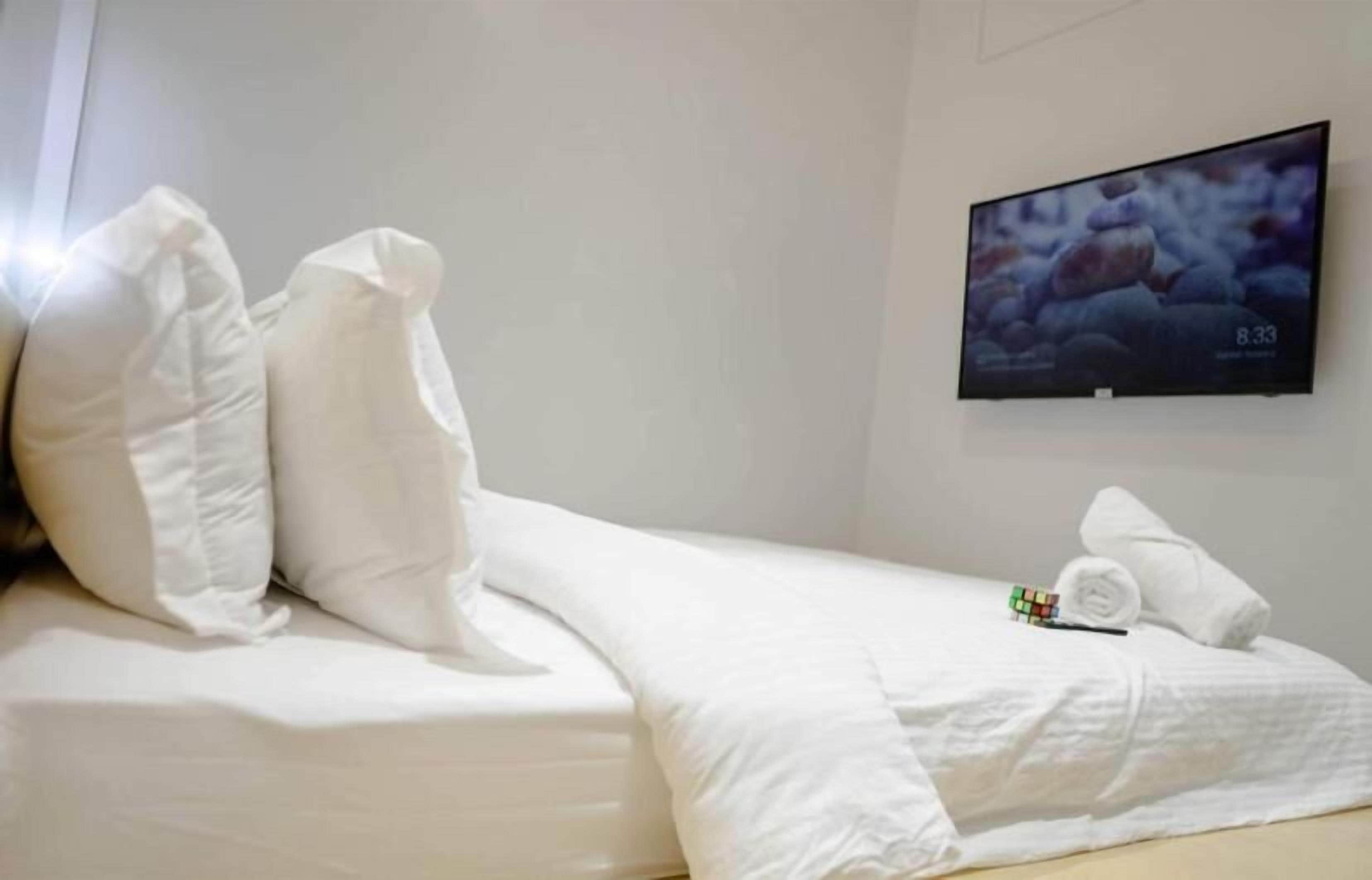 Habitación de hotel con cama, ropa de cama blanca, un televisor en la pared y un reloj que marca las 8:33.