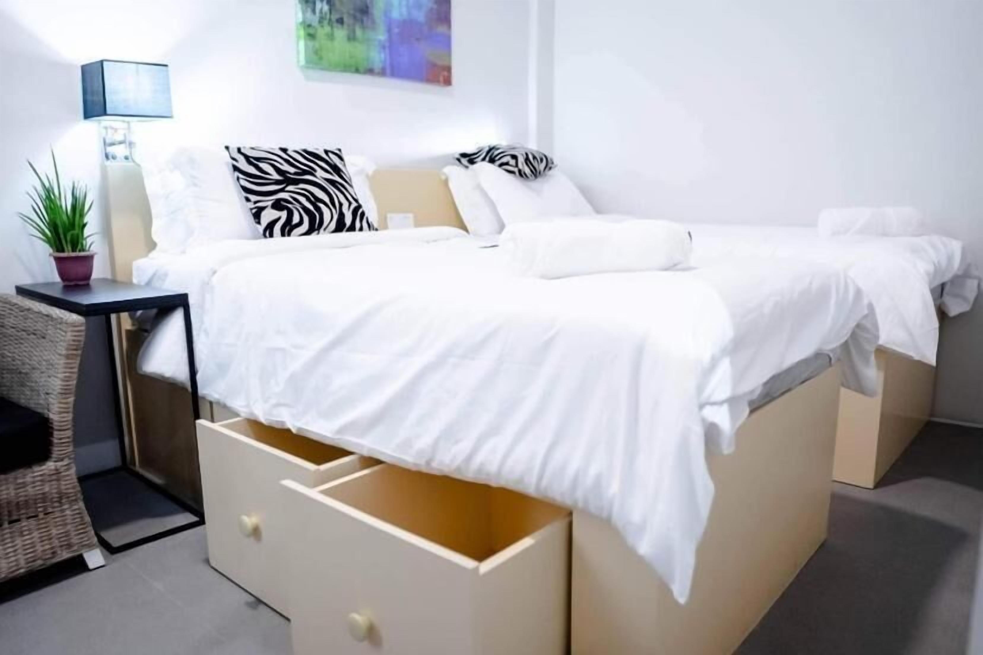 A modern bedroom with a bed, bedside tables, a lamp, and a wall-mounted artwork.