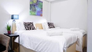 A modern bedroom with a bed, pillows, a side table, a lamp, and a wall painting. - Radlett Residences (Tuguegarao)