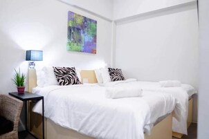 Un dormitorio moderno con cama, almohadas, una mesita de noche, una lámpara y un cuadro en la pared.