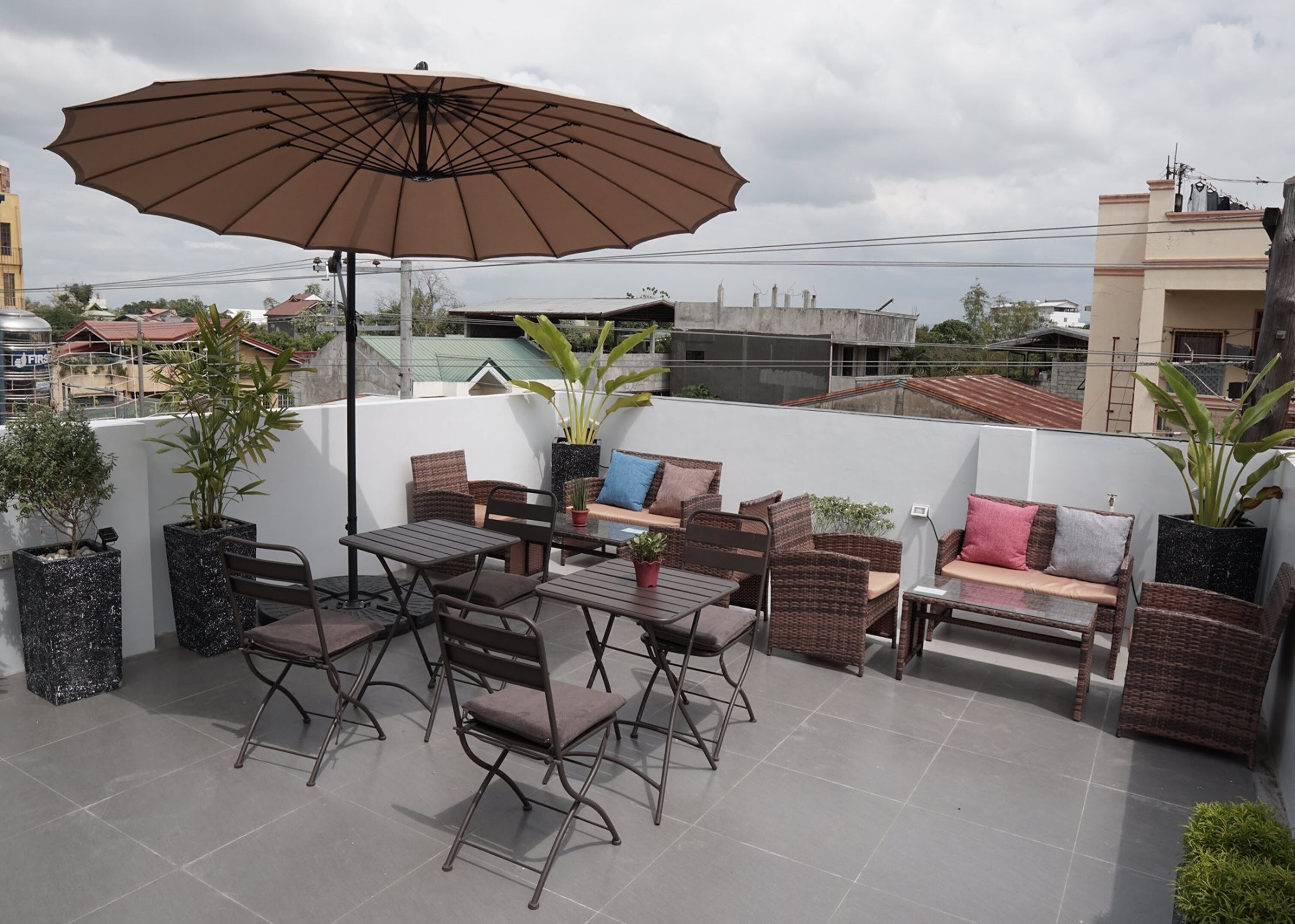 Una terraza en la azotea con mobiliario exterior, un paraguas grande y plantas en macetas.