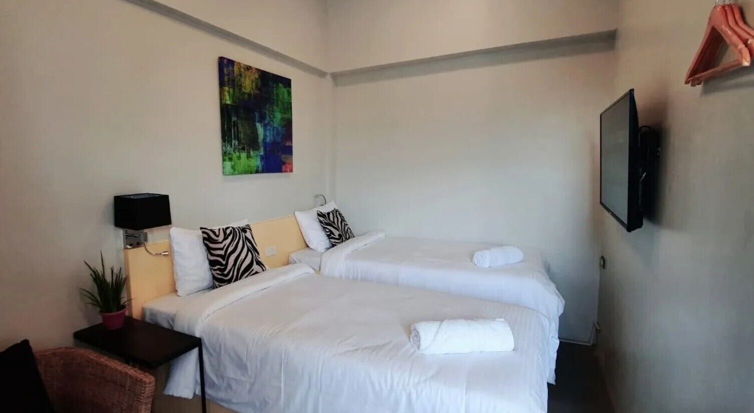 Une chambre d’hôtel avec deux lits, une télévision, un tableau et une petite table sur laquelle est posée une plante.