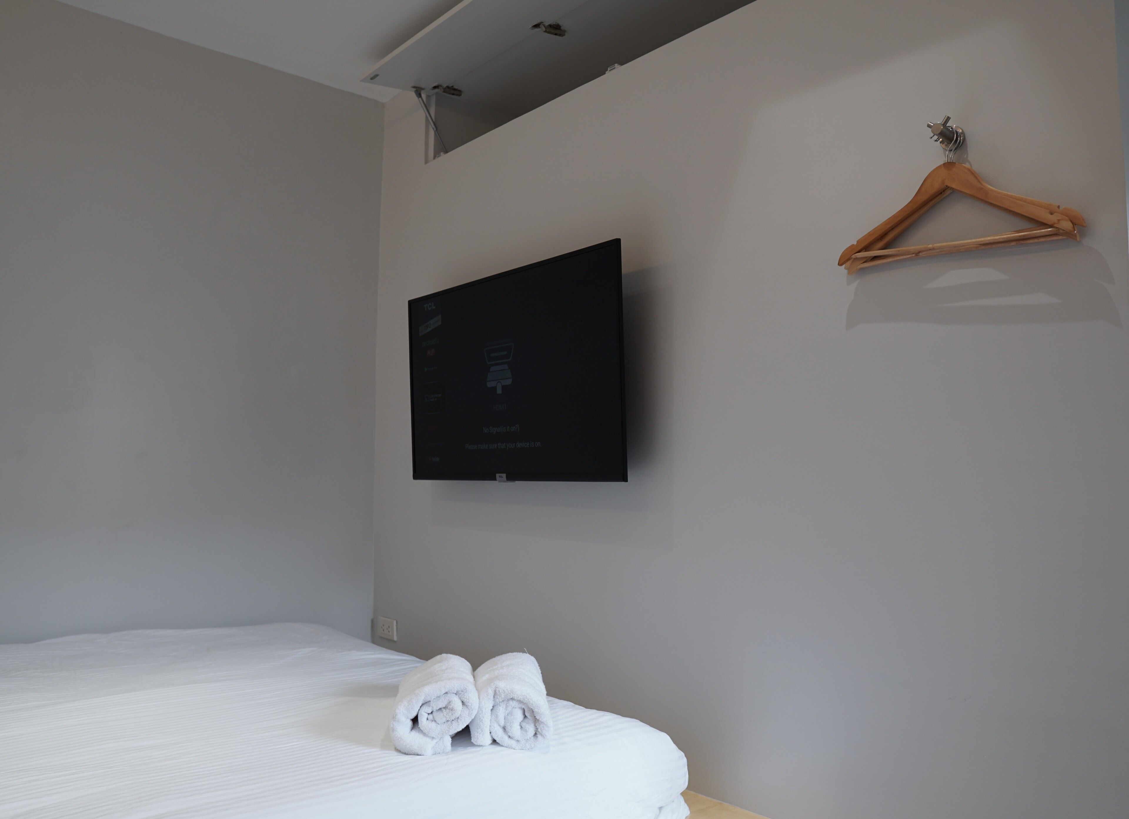 Une chambre d’hôtel avec un lit, un téléviseur fixé au mur et un cintre en bois.