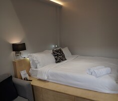 Una cama bien hecha con sábanas blancas, un cojín estampado con diseño de cebra y una toalla enrollada a un lado.