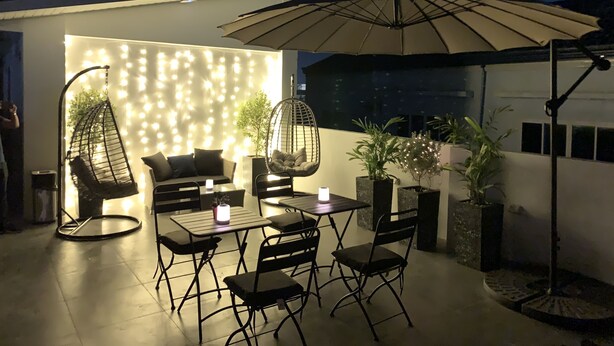 An outdoor patio area with a seating arrangement, including a sofa and chairs, a table, and a hanging chair. There are potted plants and an umbrella providing shade. - Radlett Residences (Tuguegarao)