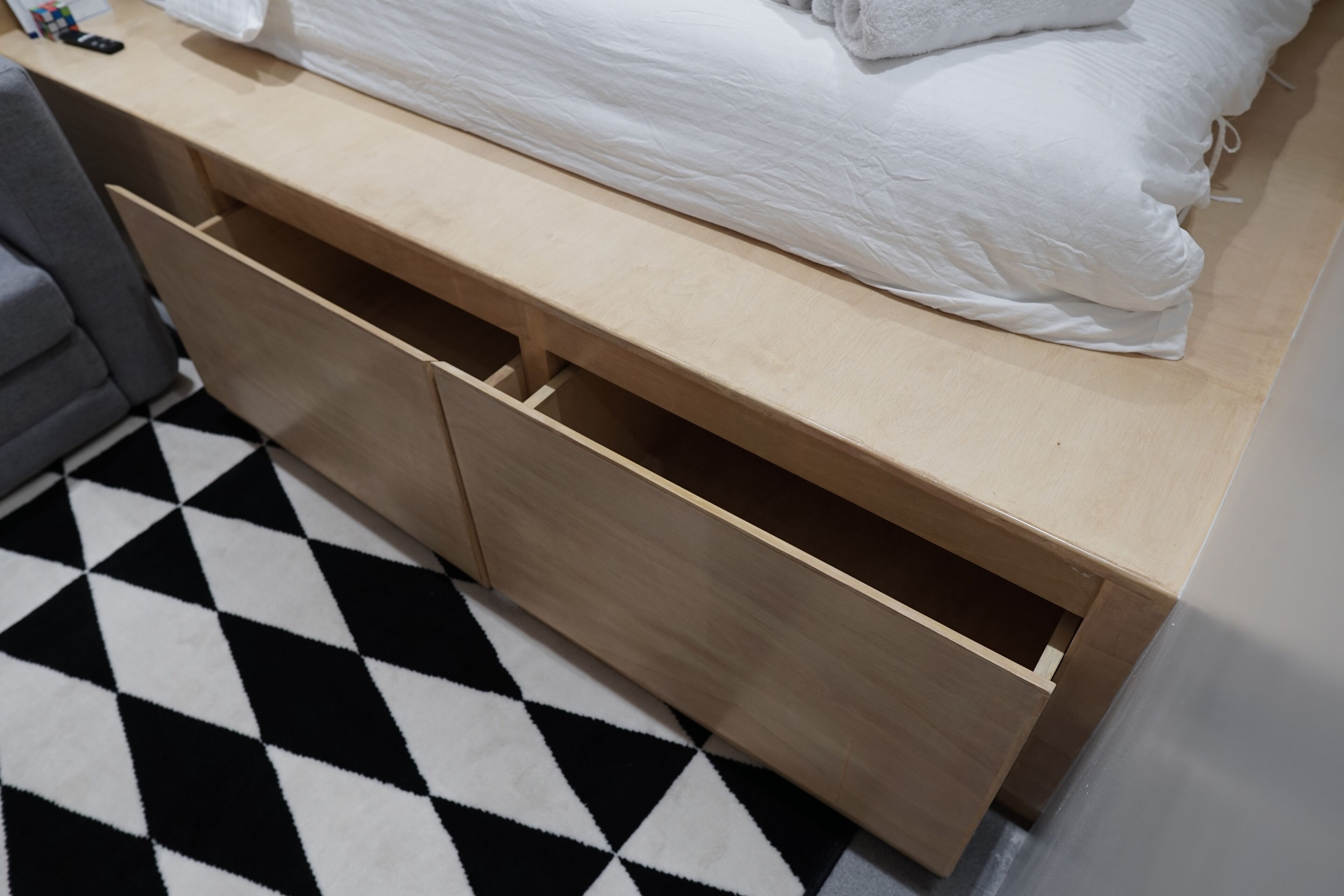A bedroom with a bed, a wooden bedside table with drawers, and a black and white checkered floor.
