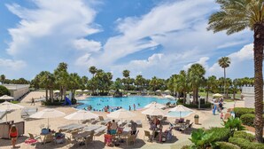 A resort with a swimming pool, lounge chairs, umbrellas, and palm trees. - 2 Bedroom Beach Front Condo (Destin)