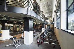 Un gimnasio de varios niveles con equipo de ejercicio diverso, incluyendo cintas de correr y máquinas de pesas, y un entrepiso con barandilla.