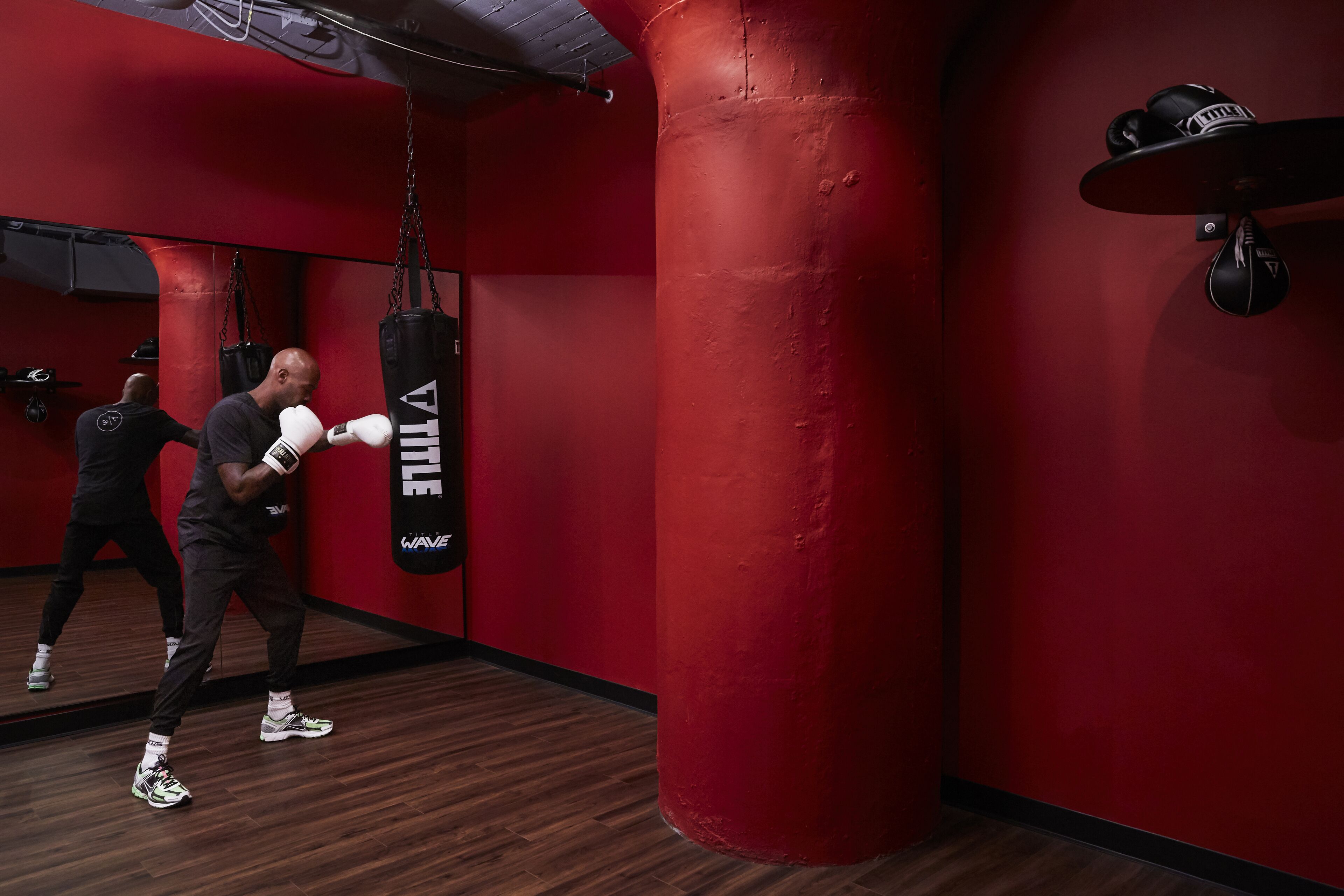 A boxing training area with a punching bag, wooden flooring, and red walls.