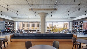 A spacious reading area with leather seating, tables, and bookshelves, featuring large windows and a view of city buildings. - Fitler Club (Philadelphia)