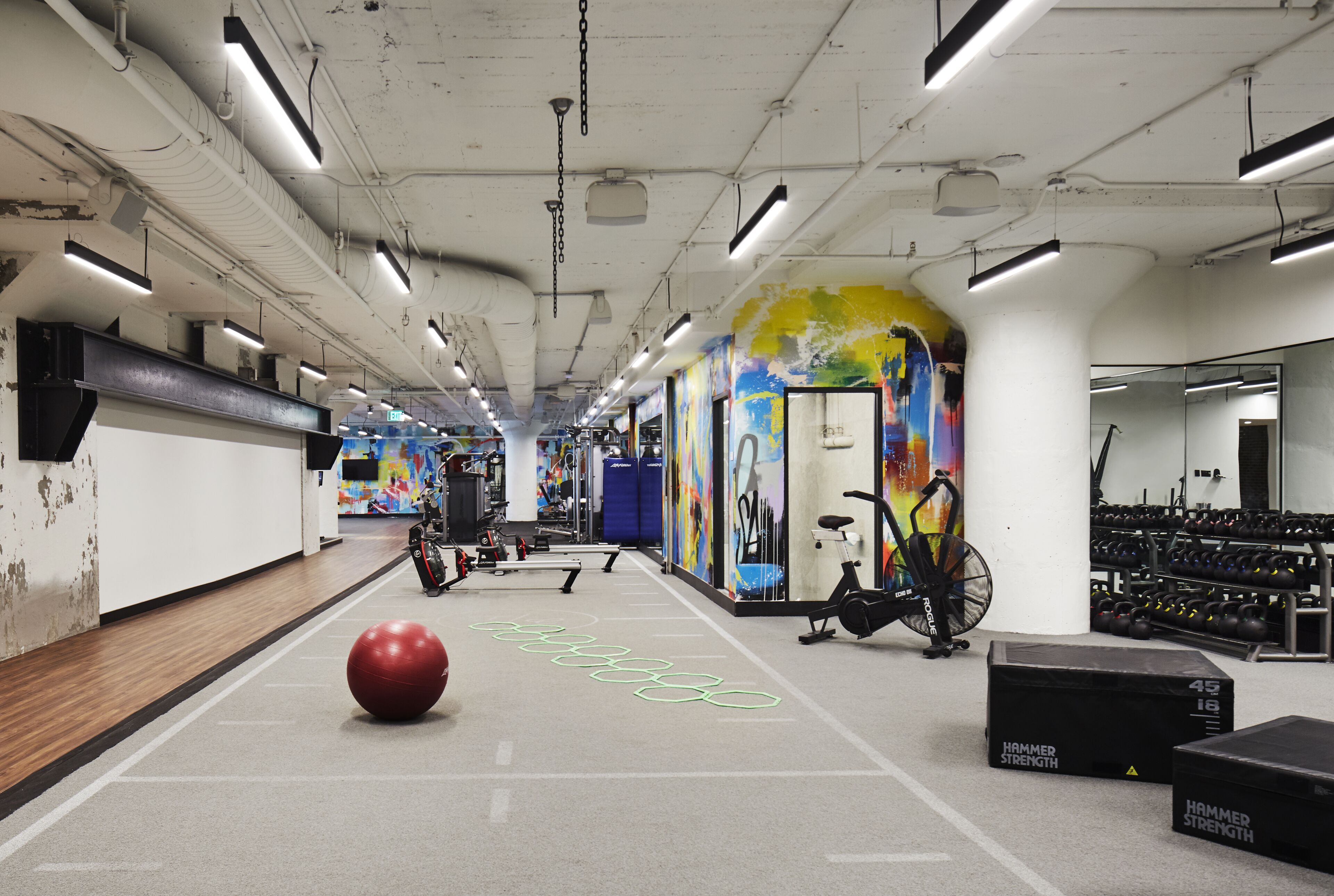 Une salle de sport équipée de matériel d’exercice, avec un ballon rouge et une fresque colorée sur le mur.