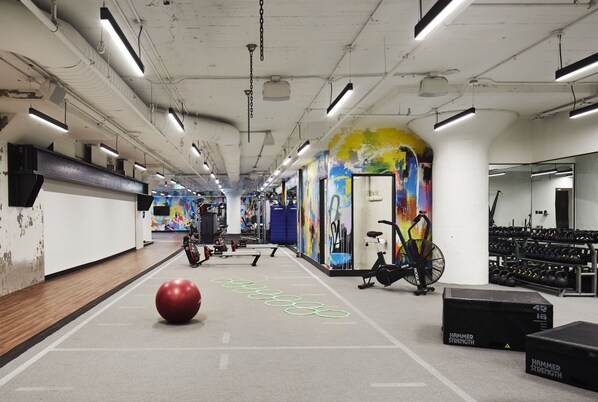 A gym with exercise equipment, a red exercise ball, and a colorful mural on the wall.