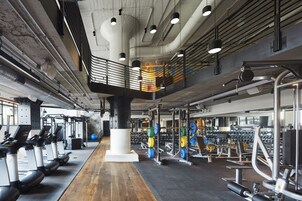 Un gimnasio con cintas de correr, máquinas de pesas y piso de madera.
