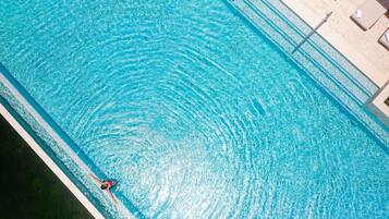 A swimming pool with a person swimming, lounge chairs, and a tiled deck.
