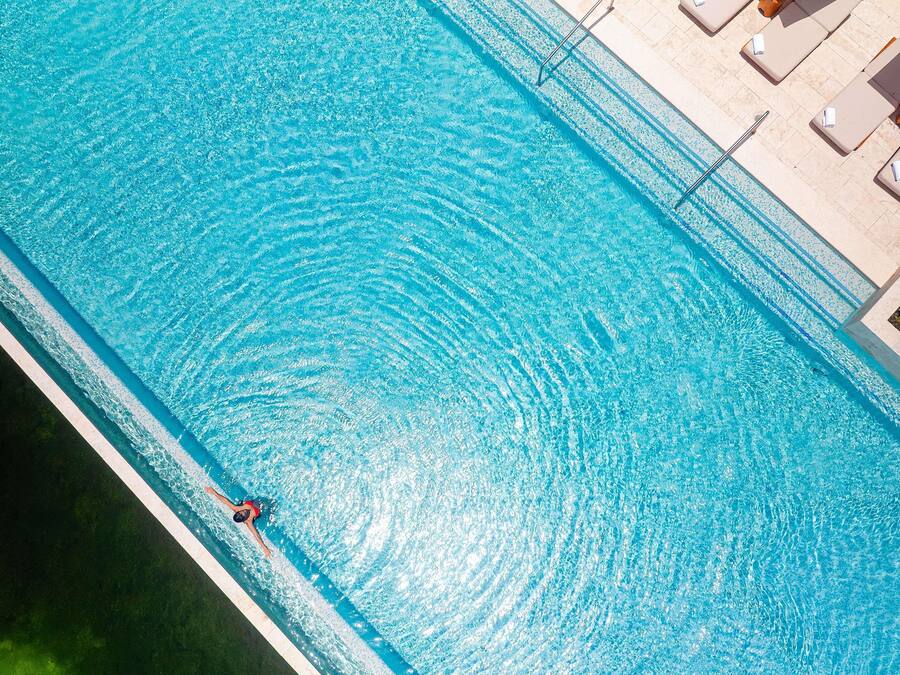 A swimming pool with a person swimming, lounge chairs, and a tiled deck.