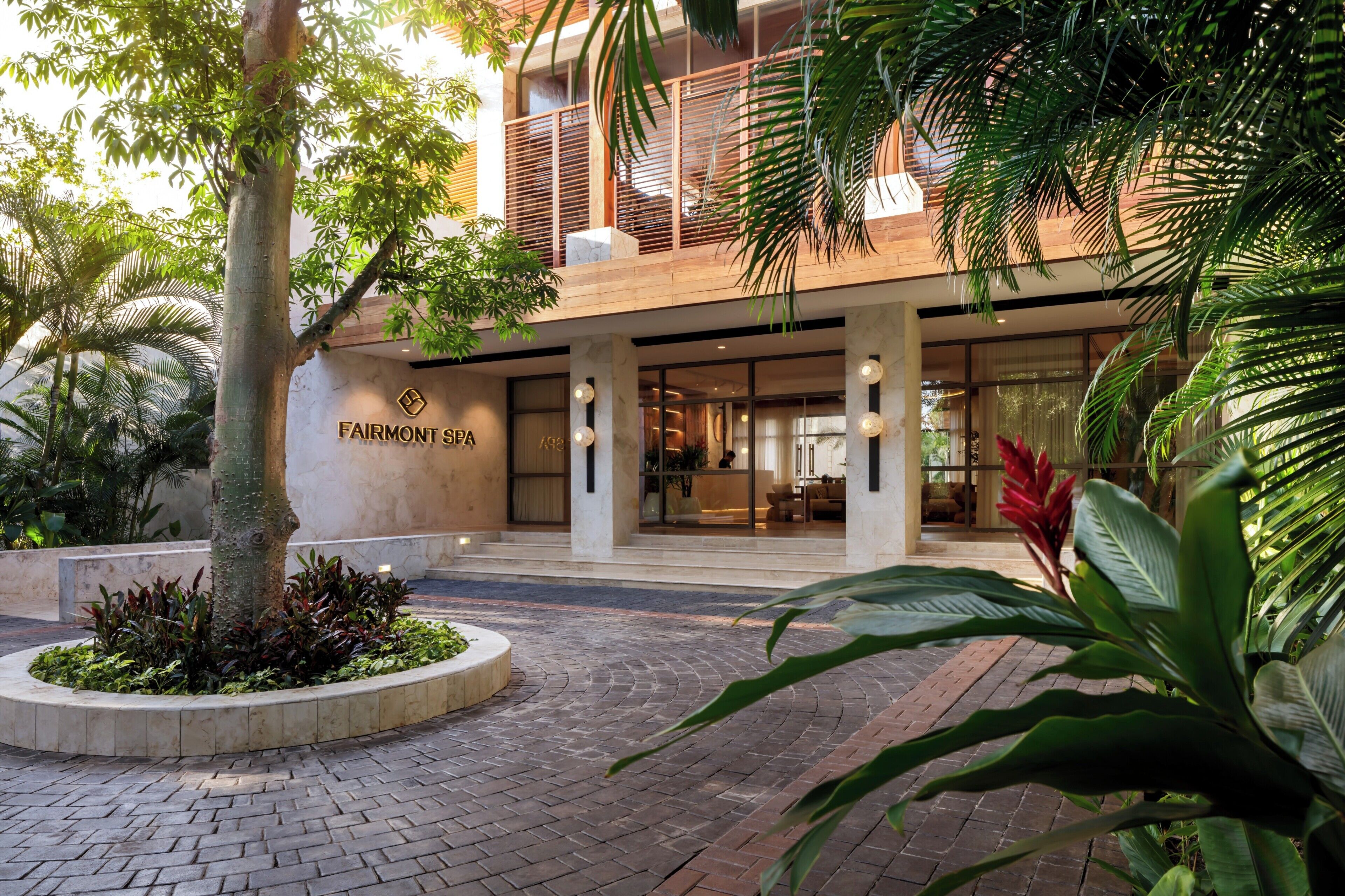 A spa entrance with a sign, a brick pathway, and surrounding greenery.