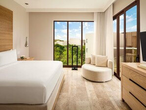 A hotel room with a large bed, a round seating area, a TV, and a view of greenery outside. - Fairmont Heritage Place Mayakoba (Playa del Carmen)