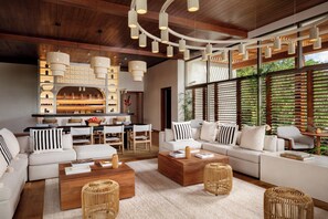 A modern living room with a large sectional sofa, a wooden coffee table, and a dining area with a bar. - Fairmont Heritage Place Mayakoba (Playa del Carmen)