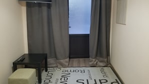 Una habitación pequeña con una cama, un televisor, una mesa y una ventana con cortinas.