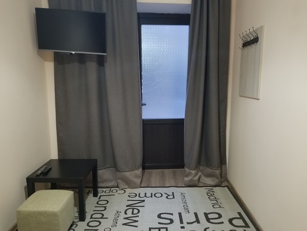 A small room with a bed, a TV, a table, and a window with curtains.