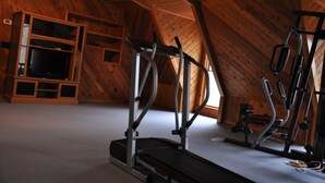 Une salle de sport équipée de matériel d’exercice, avec des murs en bois et un plafond en pente.
