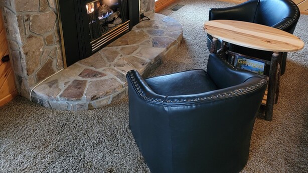 Un salon chaleureux avec une cheminée en pierre, un mur en bois, un fauteuil en cuir noir et une petite table.