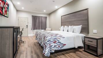 A hotel room with a large bed, bedside tables, a desk, a chair, a wardrobe, and a flat-screen TV mounted on the wall.