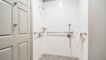 A bathroom with white tiled walls, a shower with a handheld showerhead, a grab bar, and a towel rack.