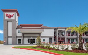 A Red Roof Inn with a modern design, featuring a prominent tower with signage, a covered entrance, and a landscaped front yard with plants and a palm tree. - Red Roof Inn Baytown (Baytown)