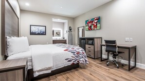 A modern bedroom with a bed, a desk, a chair, a TV, and a bathroom visible in the background. - Red Roof Inn Baytown (Baytown)